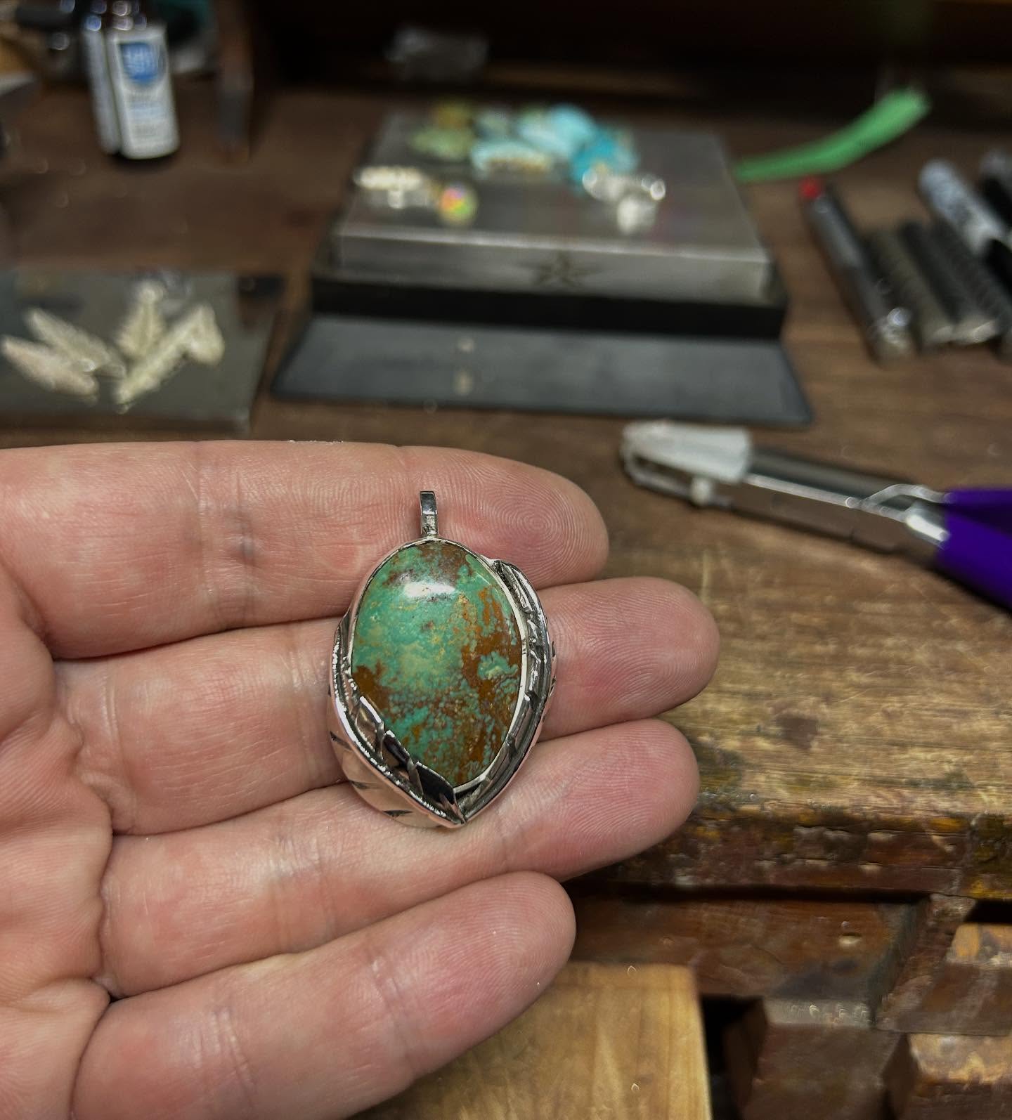 Kingman turquoise pendant with silver feather detail, in the maker's hand at the bench